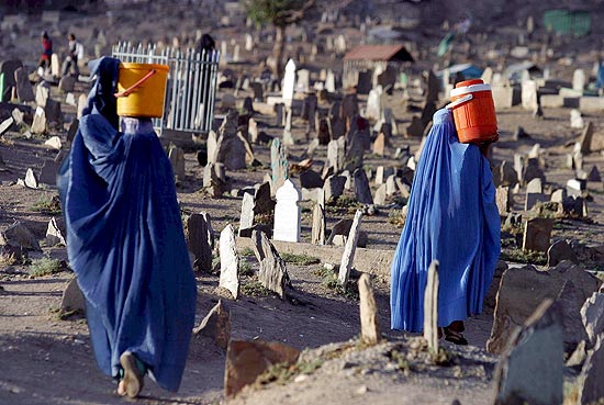 Mulheres afegãs carregam água em baldes em meio a um cemitério de Cabul; capital tem infraestrutura precária