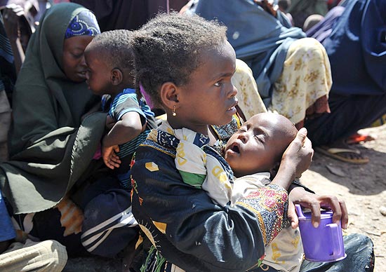 Criana carrega irm no colo, enquanto esperam por assistncia mdida em acampamento somali