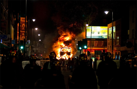 Policiais observam nibus de dois andares incendiado por manifestantes no bairro londrino de Tottenham