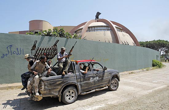 Rebeldes fortemente armados andam de carro dentro do complexo de Bab al-Aziziya, que não foi totalmente controlado