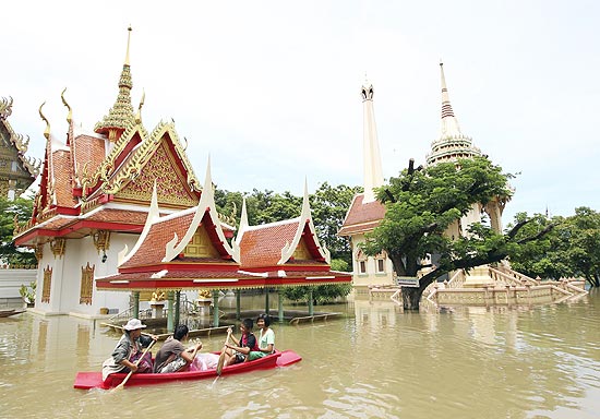 Família rema em bote, passando por templo inundado em província tailandesa; 1,5 milhão estão desabrigados