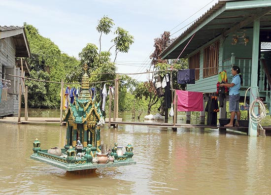 Mulher estende roupa no varal de sua casa cercada de água das inundações na Tailândia, onde 112 morreram