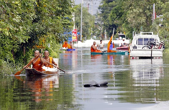Monges budistas se deslocam em botes por uma rua inundada na província de Pathum Thani, perto de Bancoc