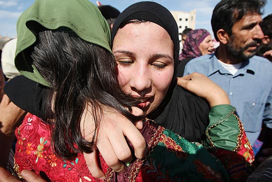 Uma prisioneira palestina  recebida por uma mulher enquanto multido aguarda centenas de presos