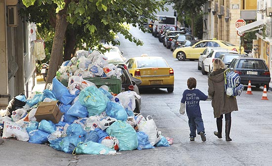 Pedestres gregos passam por entulhos de lixo em uma rua de Atenas acumulados por conta de greve