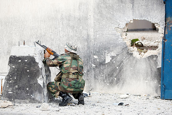 Soldado rebelde se protege durante combate com forças leais a Gaddafi na cidade de Sirte