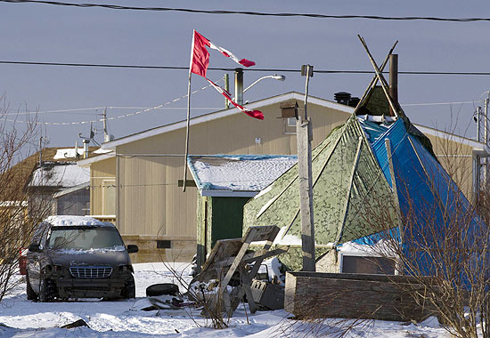 Bandeira canadense destruída balança em haste na comunidade de Attawapiskat, ao lado de cabana