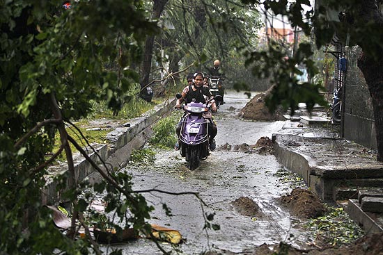 Motociclista dirige em rua onde rvores caram devido  fora do ciclone Thane, que atinge a costa da ndia