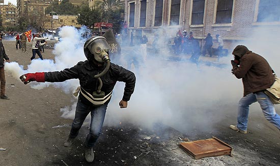 Manifestante egípcio mascarado se prepara para atirar lata de gás lacrimogêneo contra policiais