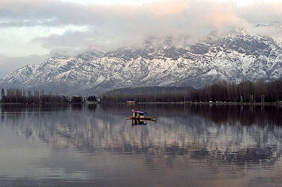 Barco navega em lago em frente a picos cobertos de neve na Caxemira
