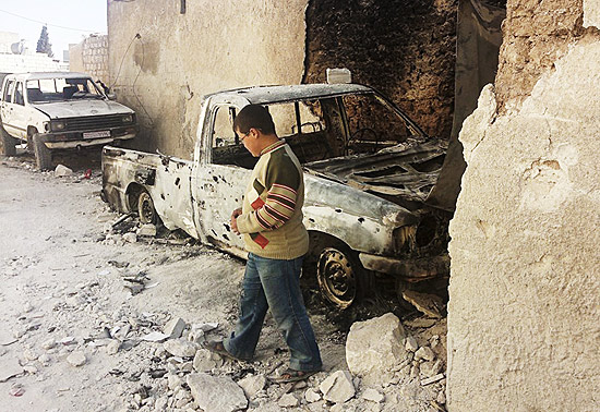Garoto ao lado de carro danificado após ataque das forças sírias na cidade de Idlib 