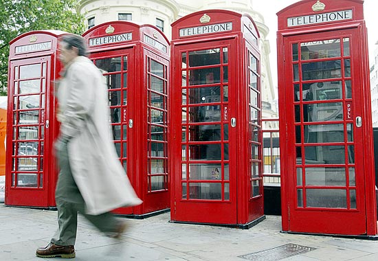 Transeunte passa diante das cabines telefônicas vermelhas em Londres, símbolo da vida britânica para os turistas 