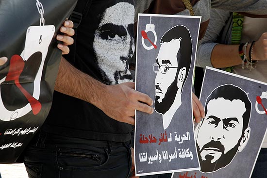 Manifestantes seguram cartazes com rostos dos presos palestinos Thaer Halahla e Bilal Thiab durante protesto em Jerusalém
