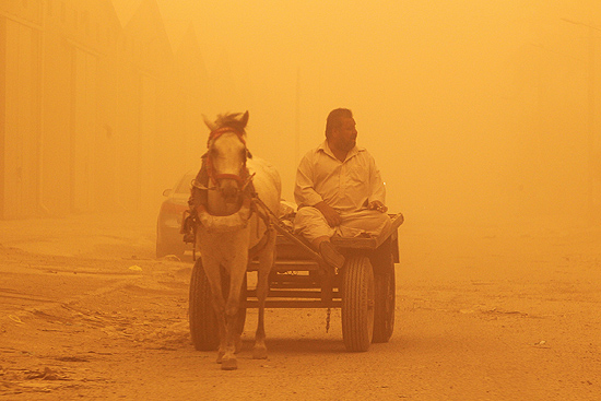 Homem tenta andar com uma carroa em rua de Bagd, afetada por tempestade de areia; aeroportos do Iraque esto fechados