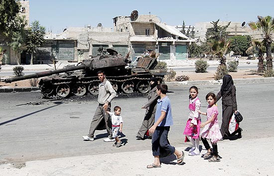 Civis sírios passam por um tanque destruído em Aleppo, no norte do país, onde confrontos continuam
