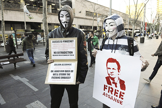 Manifestante com mscaras do coletivo hacker Anonymous segura cartaz que diz: "Augusto Pinochet: 3.000 pessoas assassinadas e torturadas, 200.000 pessoas exiladas, vendeu 370 toneladas de armas violando o embargo da ONU. No  extraditado e  posto em liberdade pelo Reino Unido. Julian Assange: Jornalista, sem acusao, com asilo poltico. Reino Unido: entregue-ou invadiremos a embaixada. No faz sentido". 