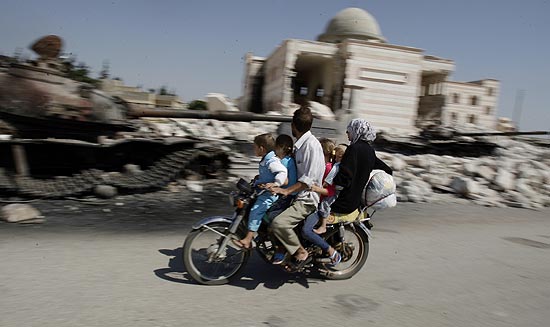 Famlia sria, em uma motocicleta, observa tanque destrudo por rebeldes em Aleppo