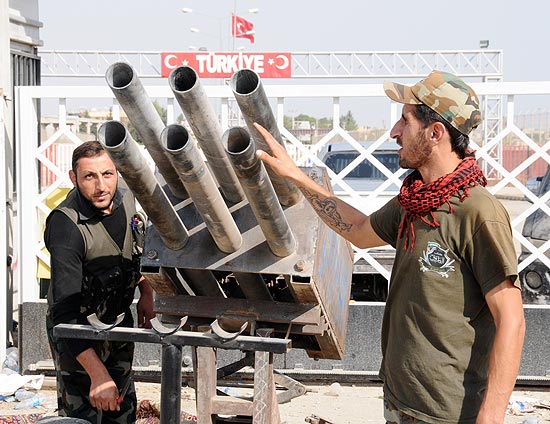 Rebeldes sírios preparam lançador de foguetes em ação na fronteira com a Turquia, nesta quinta