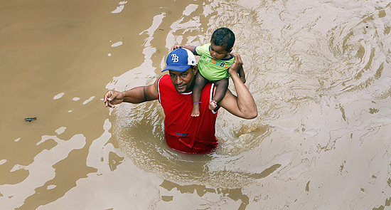 Homem carrega criança em meio a inundação provocada pelo furacão Sandy em Santo Domingo
