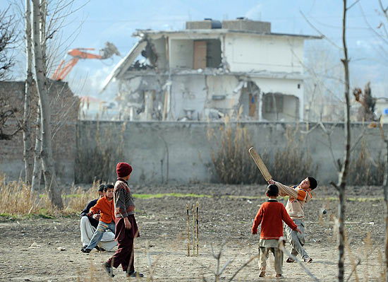 Garotos jogam crquete perto de escombros do lugar que serviu para esconder Osama bin Laden no Paquisto