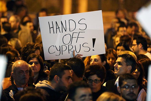 Cipriotas protestam contra UE em frente ao Parlamento na noite de quinta, com cartaz escrito "tire as mos do Chipre!"