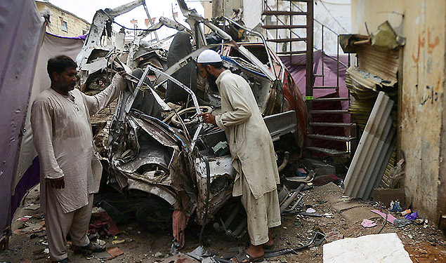 Paquistaneses observam carro destrudo pela exploso de uma bomba na cidade de Karachi, no norte do Paquisto