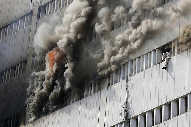 Homem se senta em janela após tentar se jogar do sétimo andar de um prédio em chamas em Lahore, no Paquistão