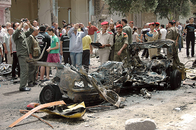 Policiais srios inspecionam restos de carro-bomba explodiu no bairro de Nozah, de maioria alauita, em Homs, na Sria