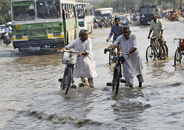 Homens tentam levar uma bicicleta aps fortes chuvas em Nova Dli; no norte da ndia, 4.000 foram soterrados