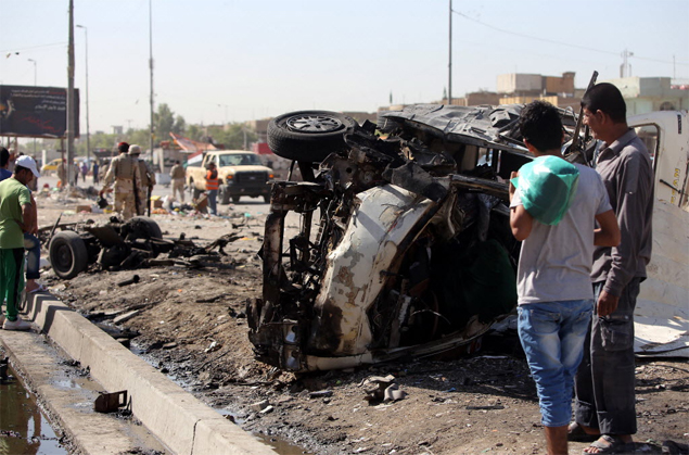 Iraquianos observam carro destrudo aps exploso de bomba em Bagd; onda de ataques causou ao menos 35 mortes no pas 