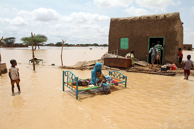Mulher e filho sentam em uma colocada em frente a uma casa em rua inundada no subrbio da capital do Sudo, Cartum