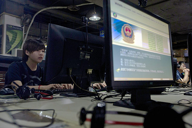 Usuários em cibercafé em Pequim; na tela, advertência sobre o uso inapropriado da rede