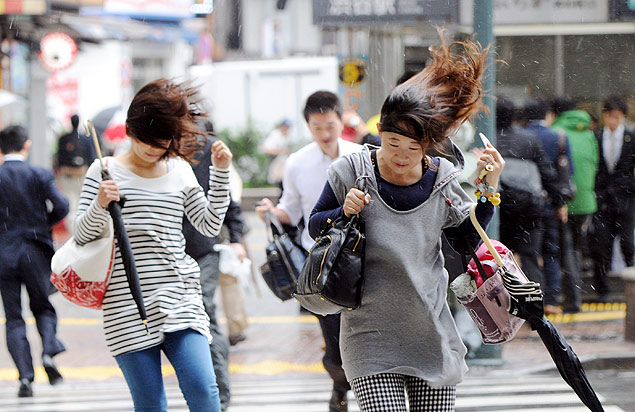 Transeuntes caminham em meio a fortes ventos na capital japonesa, Tquio, durante a passagem do tufo Wipha 