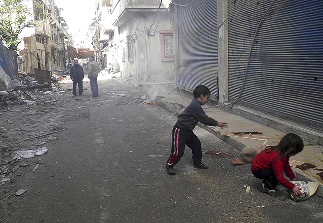 Crianças recolhem pedaços de madeira em área destruída da cidade síria de Homs, alvo de confrontos há meses