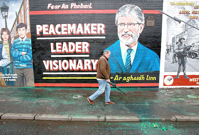 Homem passa na frente de muro com imagem do lder republicano norte-irlands Gerry Adams em Belfast