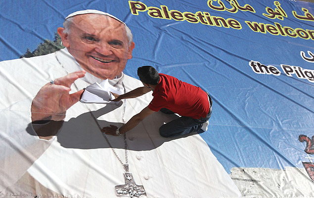 Trabalhador palestino cola cartaz em Ramallah durante preparativos para visita do papa Francisco à região