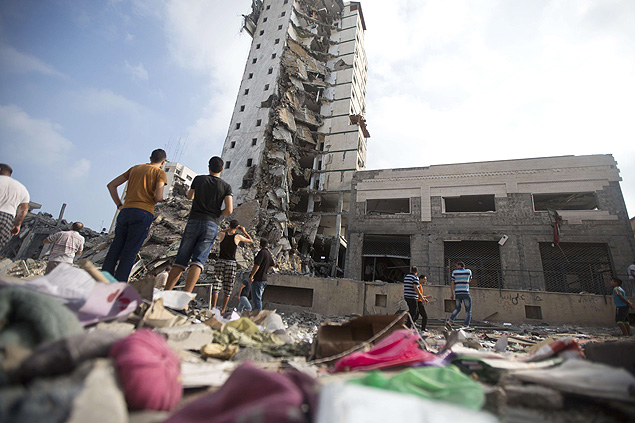 Palestinos olham prdio destrudo por bombardeio israelense na Cidade de Gaza