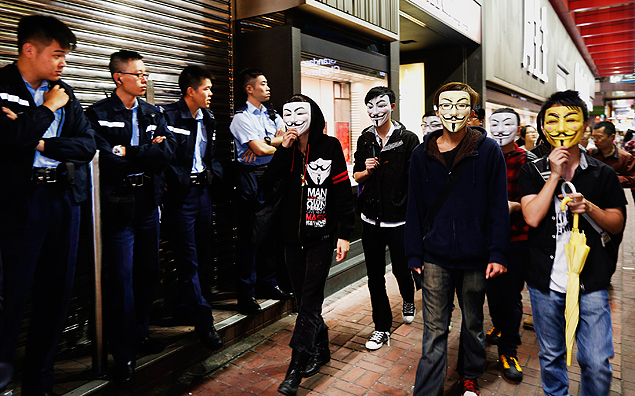 Manifestantes com mscaras passam por policiais em Mong Kok, Hong Kong