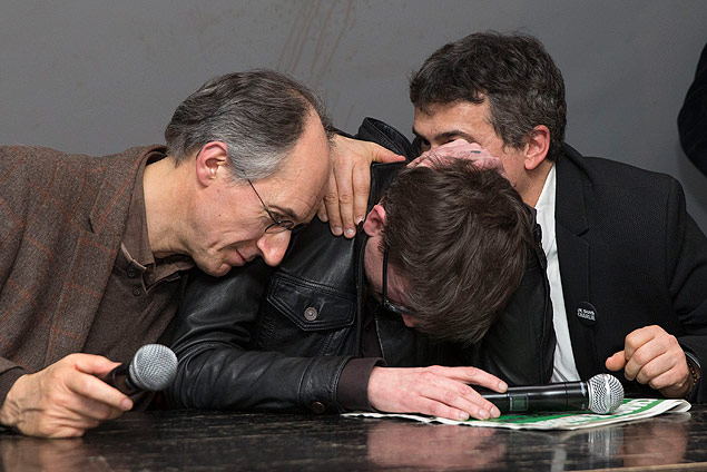 Chefe de redação do 'Charlie Hebdo', Gérard Briard (esq.) consola cartunista Luz durante coletiva
