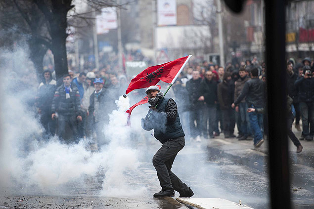 Manifestante kosovar segurando bandeira albanesa arremessa de volta uma granada de gs