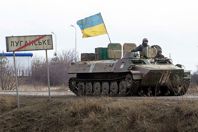 Tanque com bandeira da Ucrnia passa ao lado de placa que indica a cidade de Lugansk