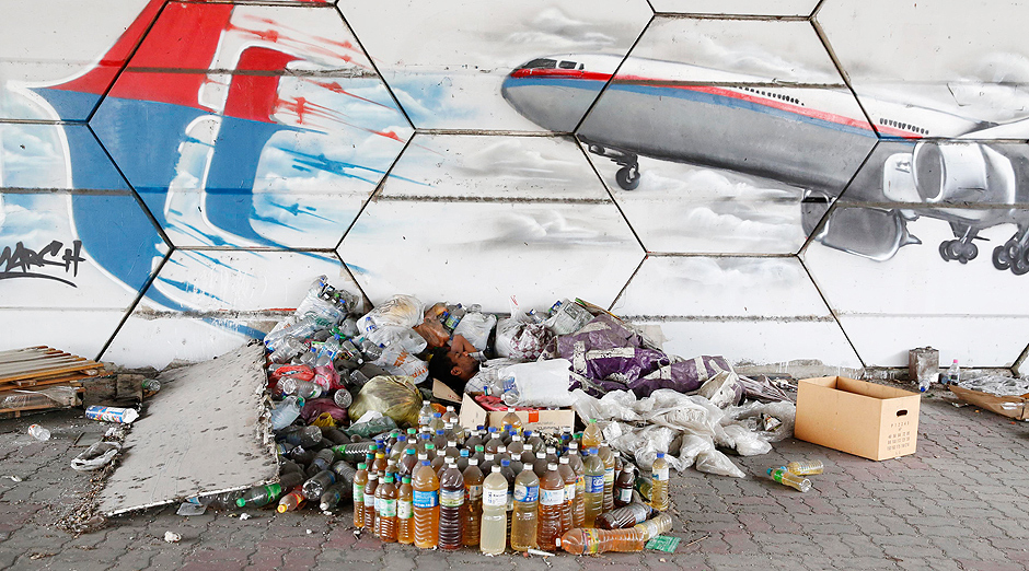 Homem dorme em frente a grafite que representa o avio desaparecido da Malaysia Airlines 