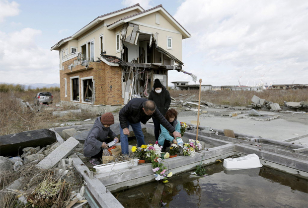 Famlia coloca flores ao lado de casa destruda por tsunami em Fukushima; japoneses prestam suas homenagens nos quatro anos da tragdia