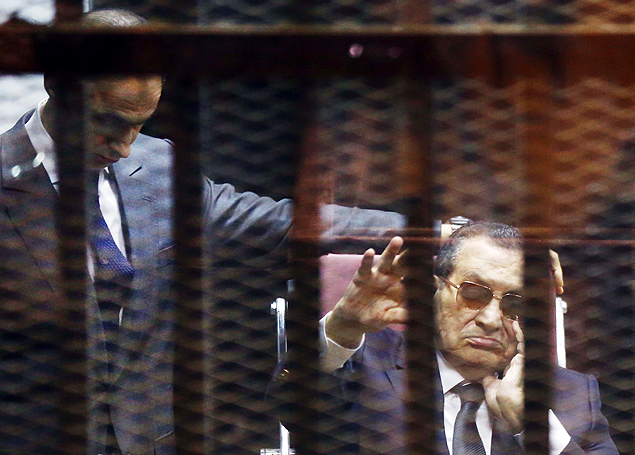Ousted Egyptian president Hosni Mubarak (R) waves from the defendant's cage next to one of his son's Gamal as they listen to the verdict in their hearing in a retrial for embezzlement on May 9, 2015 in Cairo. The Egyptian court sentenced Mubarak and his two sons to three years in prison. AFP PHOTO / MOSTAFA EL-SHEMY ORG XMIT: MS00010