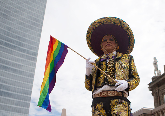 Pessoa fantasiada segura bandeira do orgulho gay em parada na Cidade do Mxico