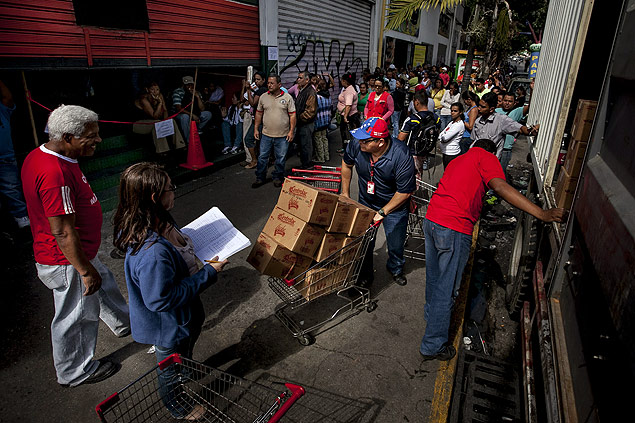 Homem descarrega produtos para mercado estatal de Caracas, e consumidores fazem fila para entrar