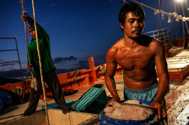 Homem trabalha descarregando barris cheios de peixes em porto de Songkhla, na Tailândia