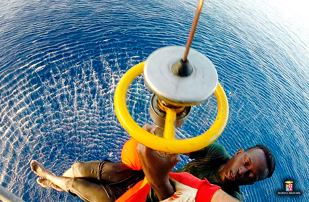 In this photo taken Tuesday, Aug. 11, and released Wednesday Aug. 12, 2015, a migrant is lifted onboard by the helicopter from the Italian Navy ship Orione, after he and another migrant were spotted clinging to a barrel, in the Mediterranean sea, between Libya and Italy. (Italian Navy VIA AP Photos) ORG XMIT: ROM104