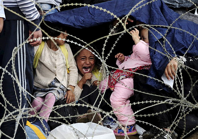 Menina chora ao tentar se proteger da chuva em Gevgelija, na Macednia, onde milhares de imigrantes tentam cruzar a fronteira rumo a pases da UE