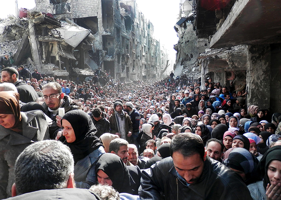 Palestinos fazem fila para receber comida no campo de refugiados de Yarmouk, em Damasco (Síria), que foi atacado pela facção Estado Islâmico neste ano